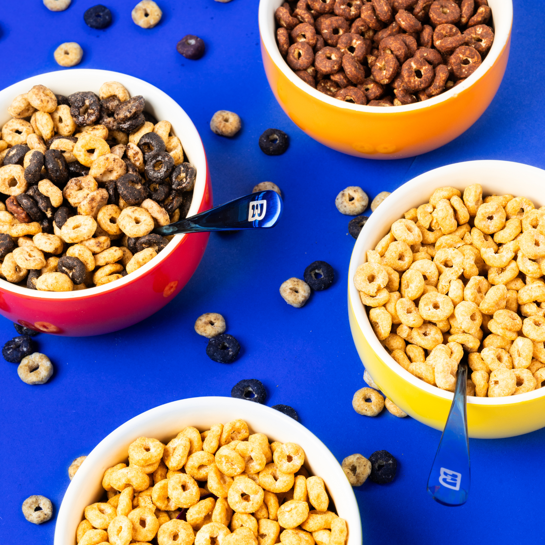 Bols Magic Morning couleur jaune, orange et rouge remplis de céréales saveur miel, chocolat, cookie and cream, peanut butter. Presentation coloree sur fond bleu vif, mettant en avant des cereales saines, riches en proteines et faibles en sucre.