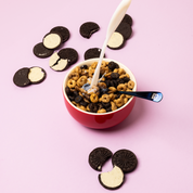 Un bol de cereales Magic Morning saveur Cookie & Cream avec du lait verse, accompagne de biscuits au cacao et a la creme sur un fond rose pastel. Un petit-dejeuner sain, proteine, faible en sucre et riche en fibres pour bien commencer la journee.